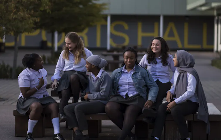 Group of girls in school uniform sitting on a bench.