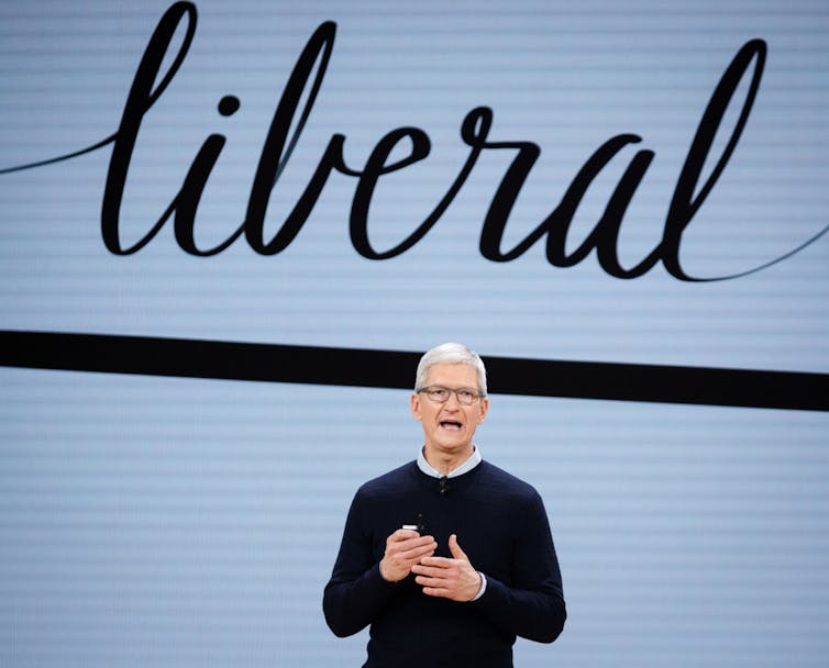 Tim Cook standing below a sign that says 'liberal'