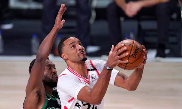 A basketball player prepares to throw the ball with another player behind him.