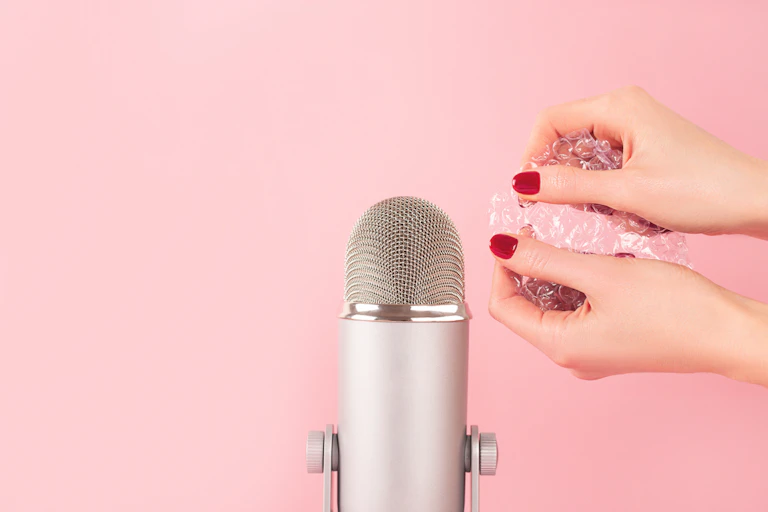 Woman with painted nails pops bubble wrap beside a microphone.
