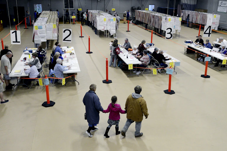 Poll workers sit at long tables checking in voters in a cavernous, auditorium-type space