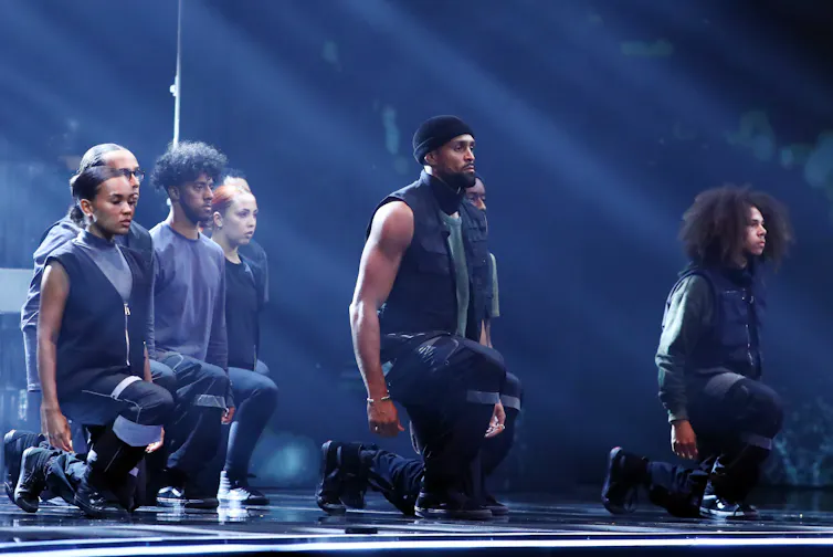 Group of dancers in black kneeling on one knee with their eyes closed.