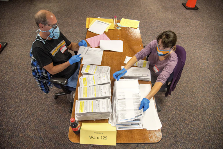 People in masks and gloves handle ballots.