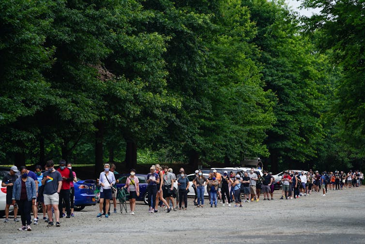 Dozens of people in masks standing outside in a long line