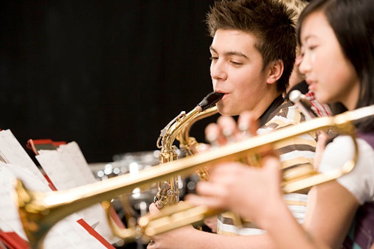 Two students play the saxophone while reading sheet music.