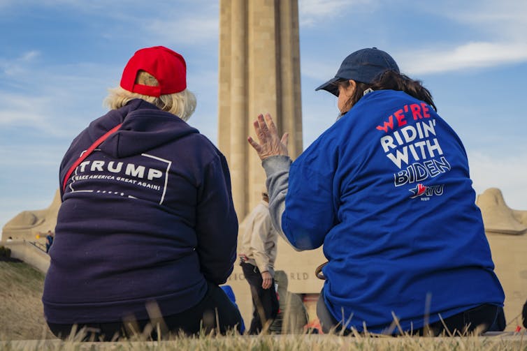 Two women conversing with their backs to the camera, one wearing a Trump shirt and the other a Biden shirt.