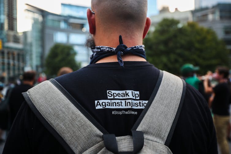 Back of a man whose t-shirt reads 'Speak up against injustice'