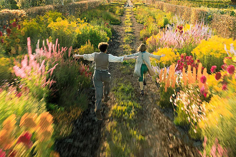 Film still: two children run through a flowering garden