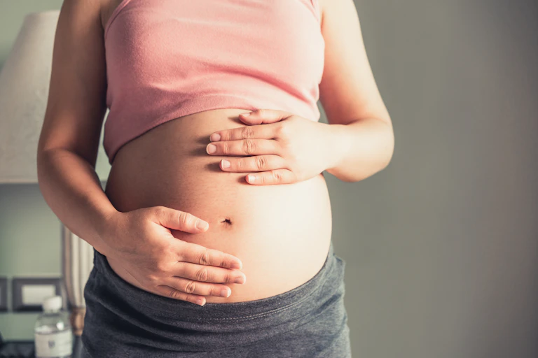 A pregnant woman has her hands on her belly.