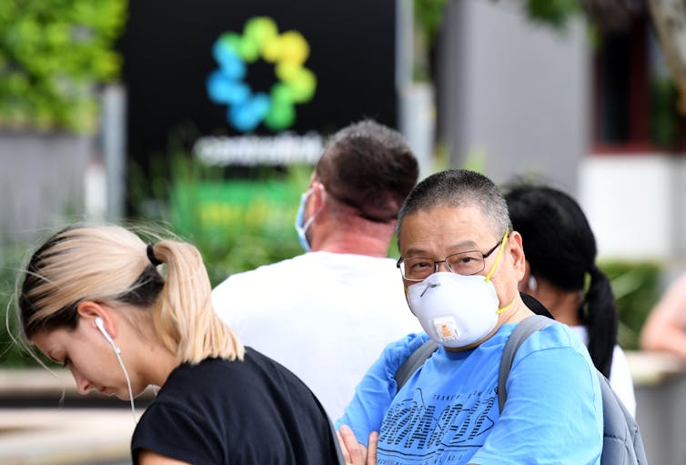 Man wearing mask lines up outside Centrelink office.