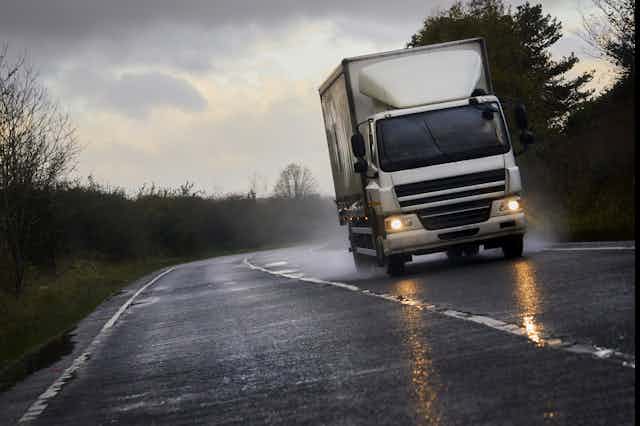 A white lorry speeds down a wet road.