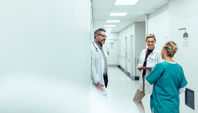 Two doctors and a nurse talk to each other in a hospital hallway.