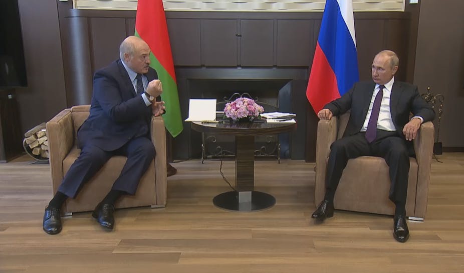 Alexander Lukashenko and Vladimir Putin sitting in chairs with their flags behind.