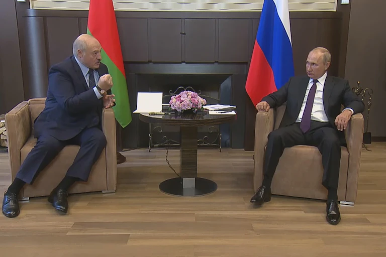 Alexander Lukashenko and Vladimir Putin sitting in chairs with their flags behind.
