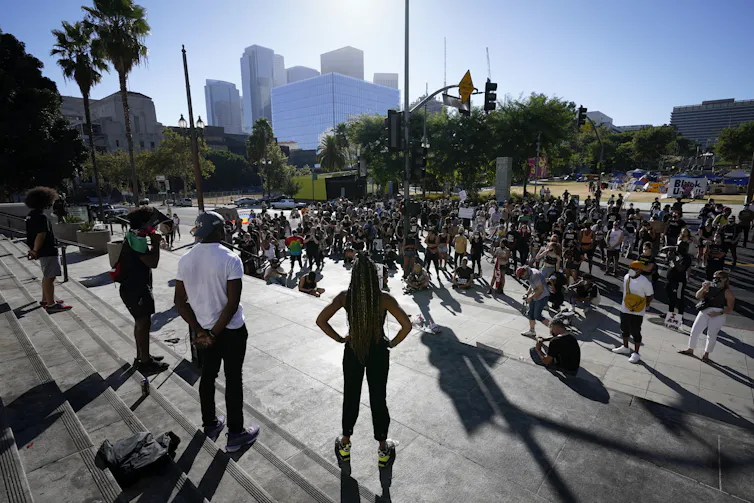 People stand in the sun with shadows cast in front of them.