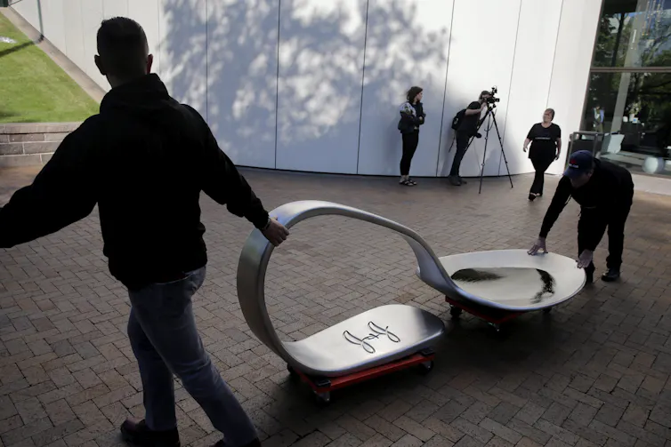Two people wheel a giant opioid spoon.