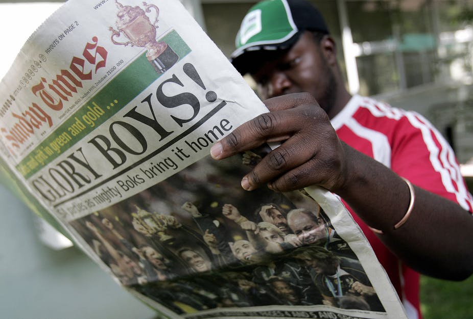 A man wearing a green sports cap and read T.shirt reads a copy of South Africa's Sunday Times