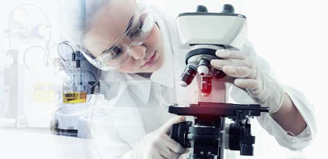 Una mujer con bata y guantes blancos manipula un microscopio.