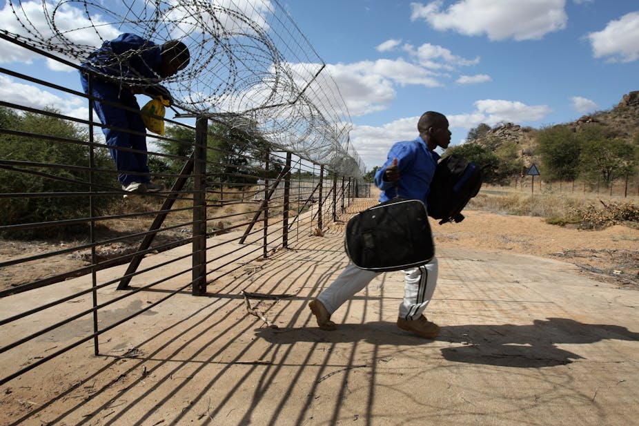 A man carries a backpack after jumping a barbed wire fence marking the border between South Africa and Zimbabwe while another prepares to join him