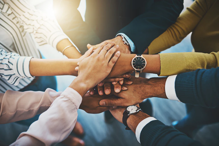 Closeup shot of a group of businesspeople joining their hands together in a huddle.