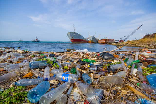Plastic litter floats on sea surface, large ship in background