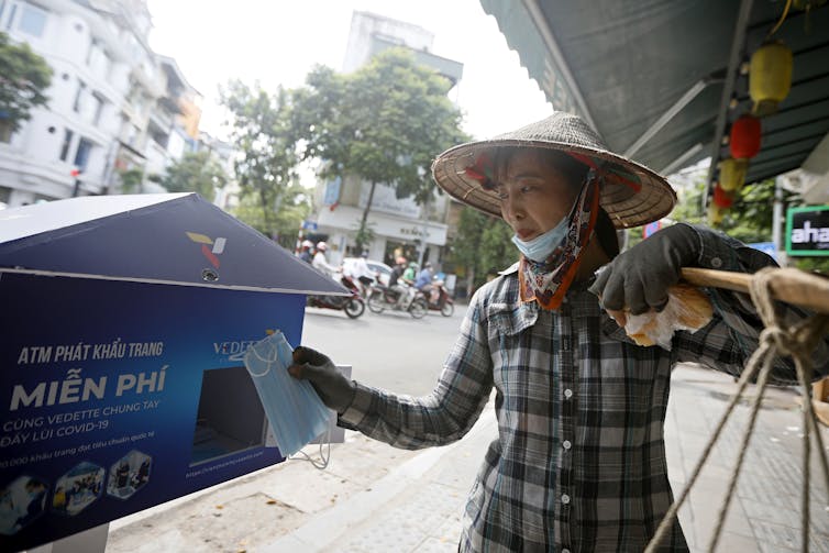 A woman wearing a pointed hat collects a mask from a street machine.