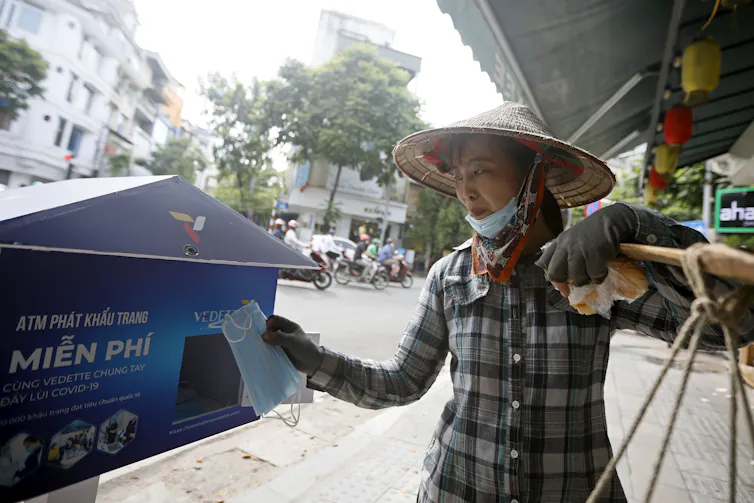 A woman wearing a pointed hat collects a mask from a street machine.