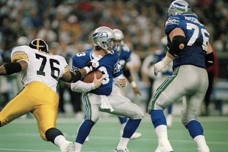 a football player grabs another player from the opposing team while a third football player watches