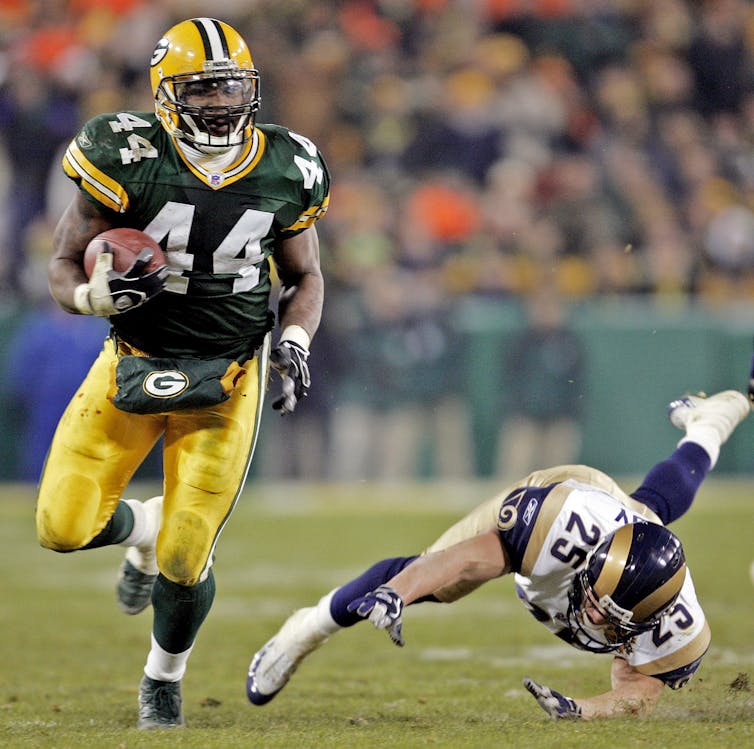 a player holding a football runs past a player from another team