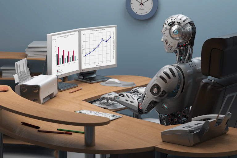 A robot sitting at a desk in front of a computer.