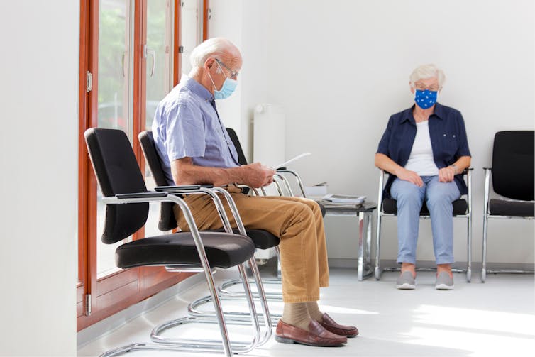 A man and a woman wearing masks sit in a waiting room.