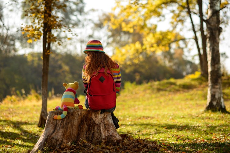 A girl sitting on a tree stump and talking to her toy cat