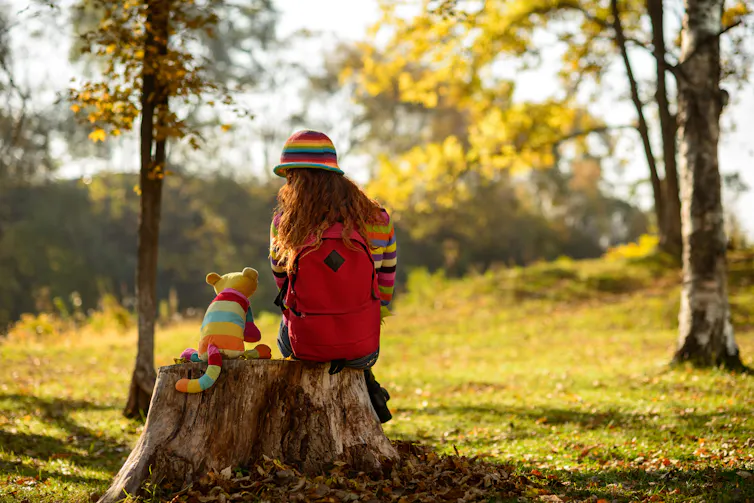 A girl sitting on a tree stump and talking to her toy cat
