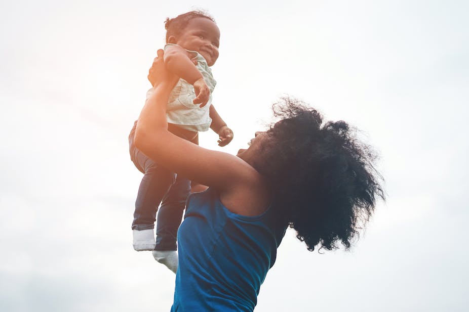 A woman holds a toddler aloft, both are smiling and having fun