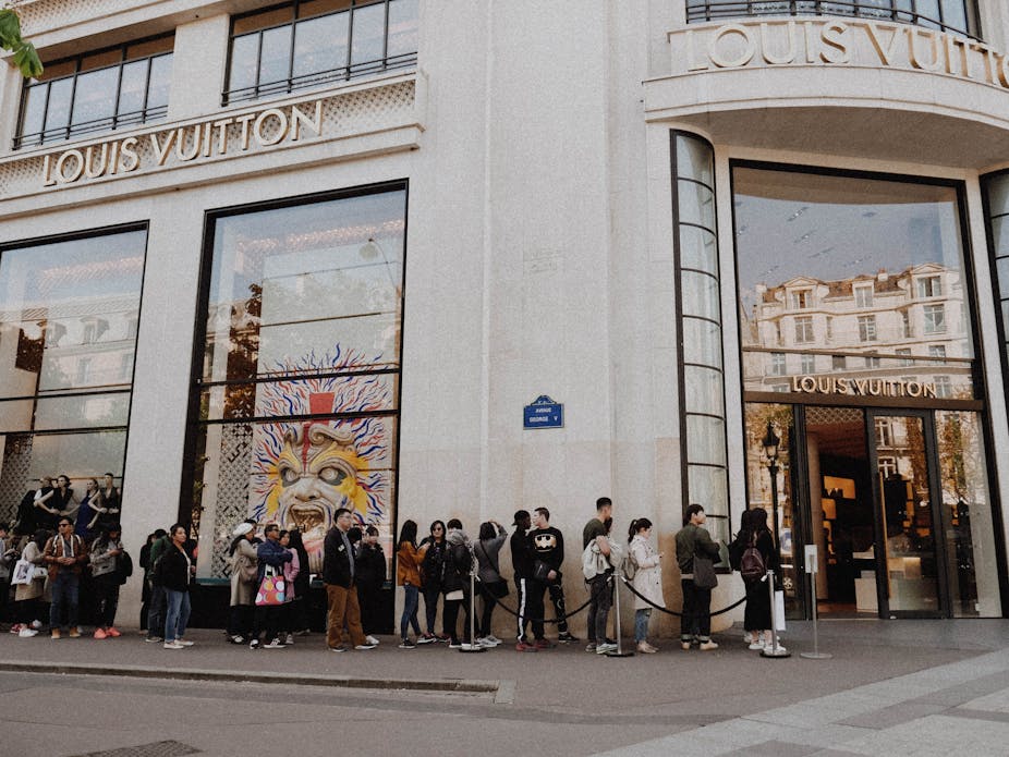 Line of people waiting outside Louis Vuitton store on street in Paris.