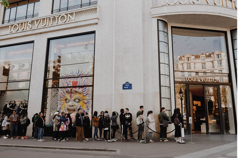 Line of people waiting outside Louis Vuitton store on street in Paris.
