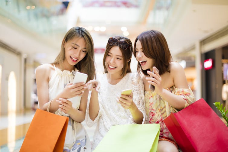 Three women smiling at smartphone in shopping mall.