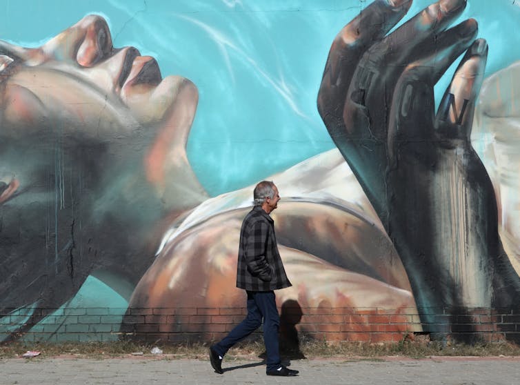 A man walks past a street art mural depicting a blonde-haired woman lying calmly on her back underwater.