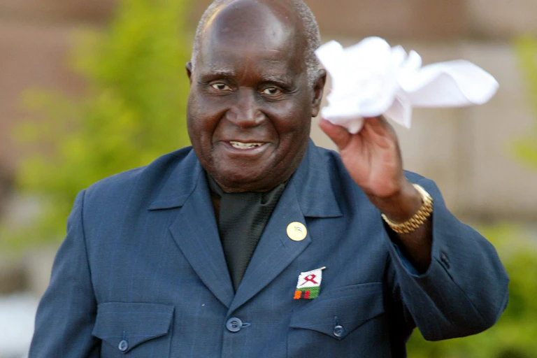 Elderly man in a suit and cravat, smiling, waving a white handkerchief