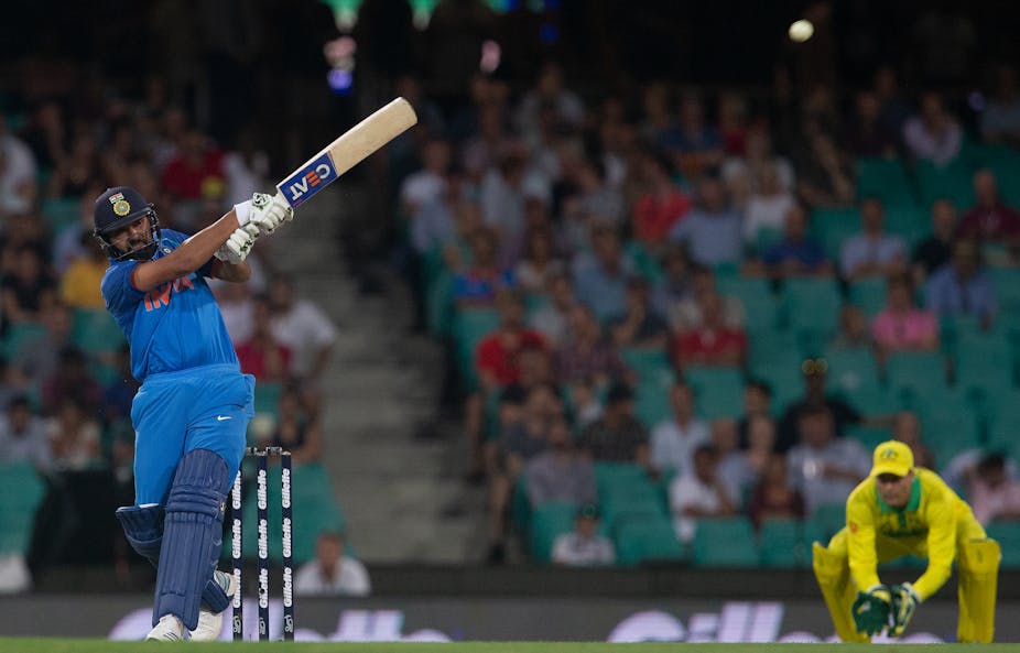 Rohit Sharma hits cricket ball with man crouching behind.