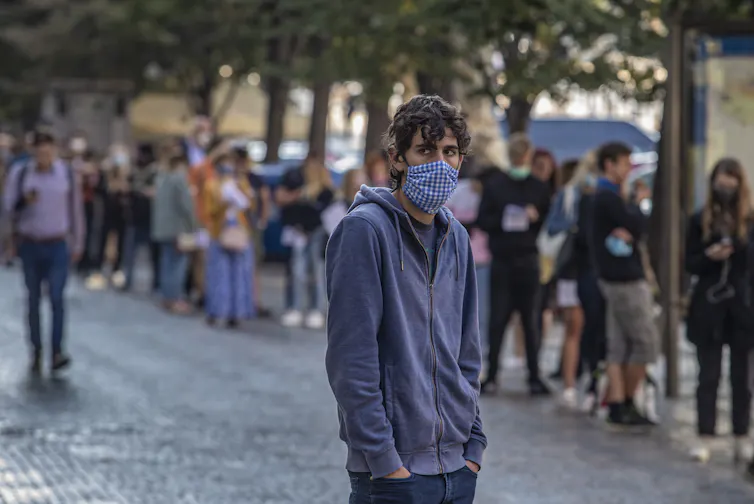 A man in a mask standing in front of a long queue of people, also in masks.