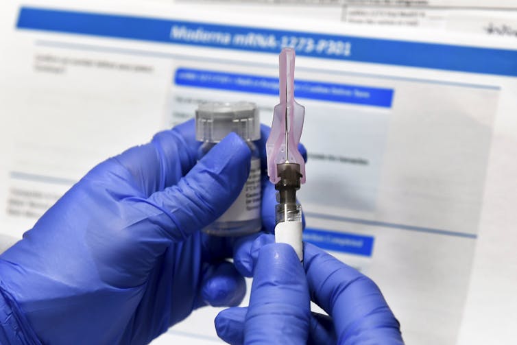 Gloved hands holding a syringe of the Moderna vaccine.