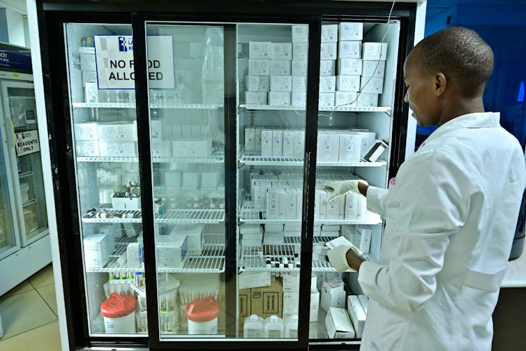 A man in a lab coat stands in front of a freezer filled with medical supplies.