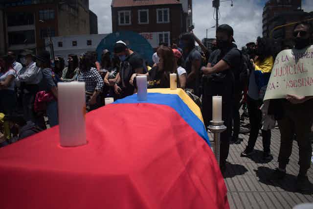 Ataúd cubierto por la bandera de Colombia y tres velas.