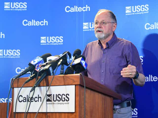 Man speaks at a podium labelled Caltech and USGS