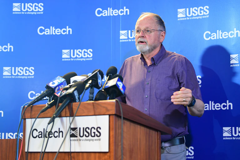 Man speaks at a podium labelled Caltech and USGS