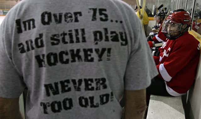 A man at a hockey rink wears a t-shirt that says I'm over 75...and still play HOCKEY! NEVER TOO OLD!