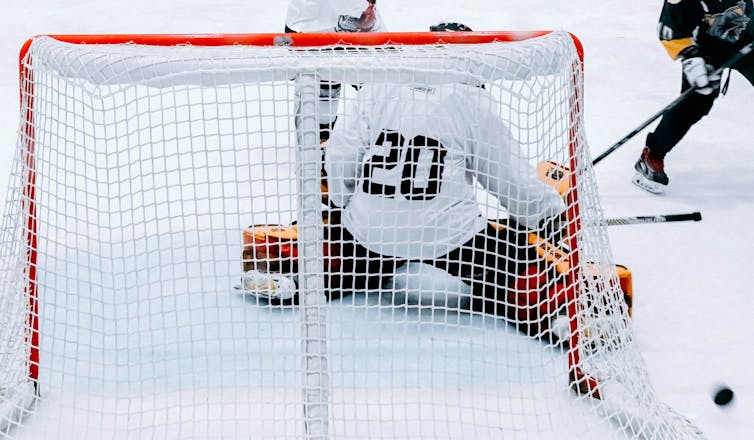 A hockey player shoots and misses as a goalie makes a save.