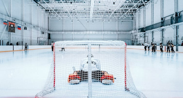 A goalie stretches in the foreground as hockey players in the background get ready to practice.