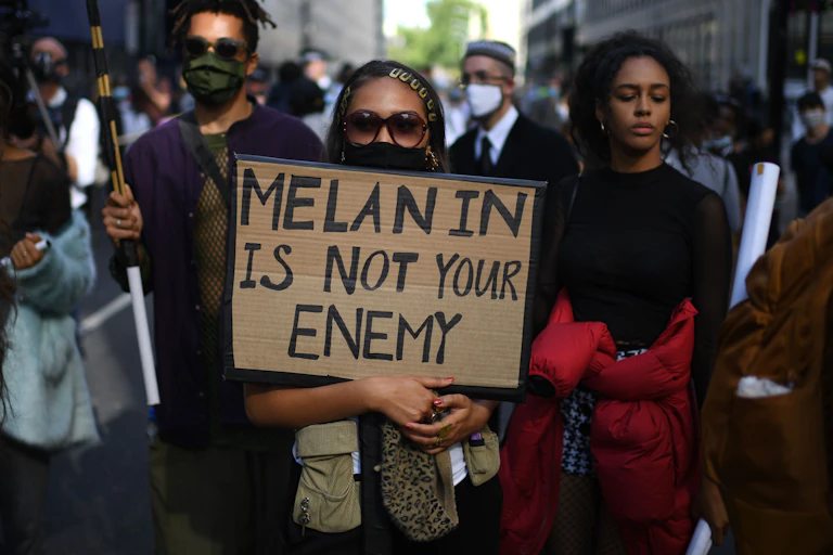Black Lives Matter protestors in New York, a woman in sunglasses in the foreground holding a placard that reads, 'Melanin is not your enemy'
